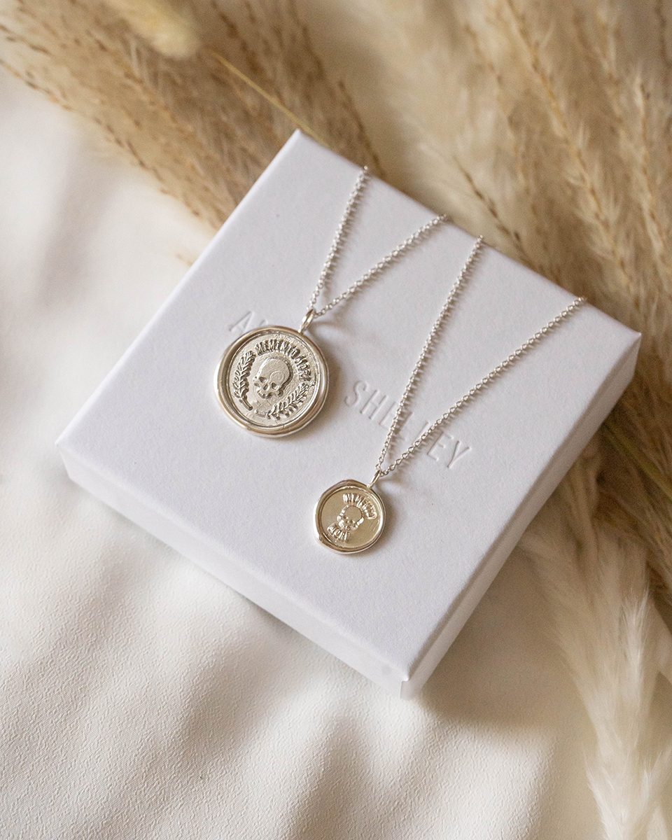 Large and small memento mori pendants laying on white jewelry box.
