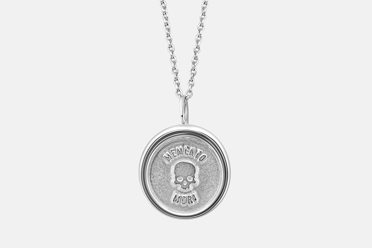 small memento mori pendant in sterling silver on a white background.