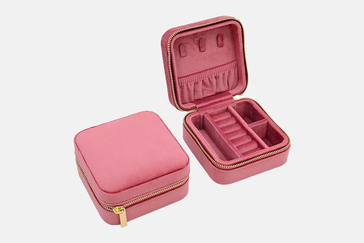 A square pink velvet jewelry case shown zipped shut and opened to show compartments for rings, hanging necklaces, and earrings.