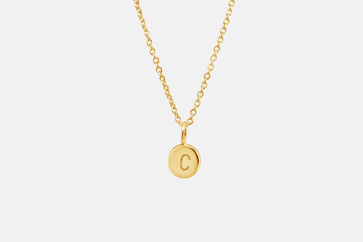 Small gold letter pendant on a chain shown on a model's neck.