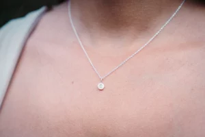 Small silver letter pendant on a chain shown on a model's neck.