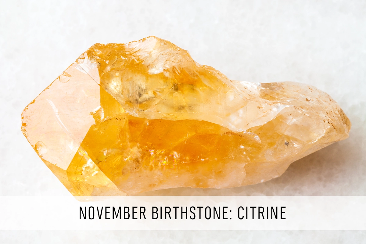 A photo of a yellow citrine crystal against a white background with the text November Birthstone: Citrine.